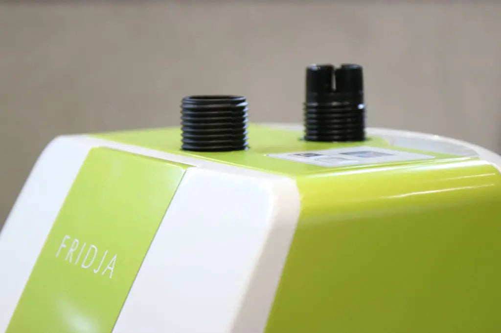 Close-up of a green and white appliance labeled FRIDJA with two black threaded nozzles on top, likely for attachments or hoses; a small digital display is partly visible.