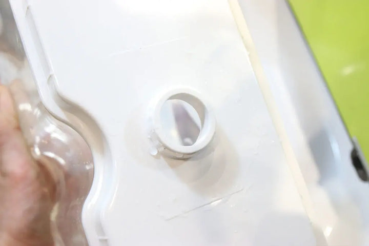 Close-up of a white plastic container with a round, open spout on top, set against a green background. The spout appears clean and unused.