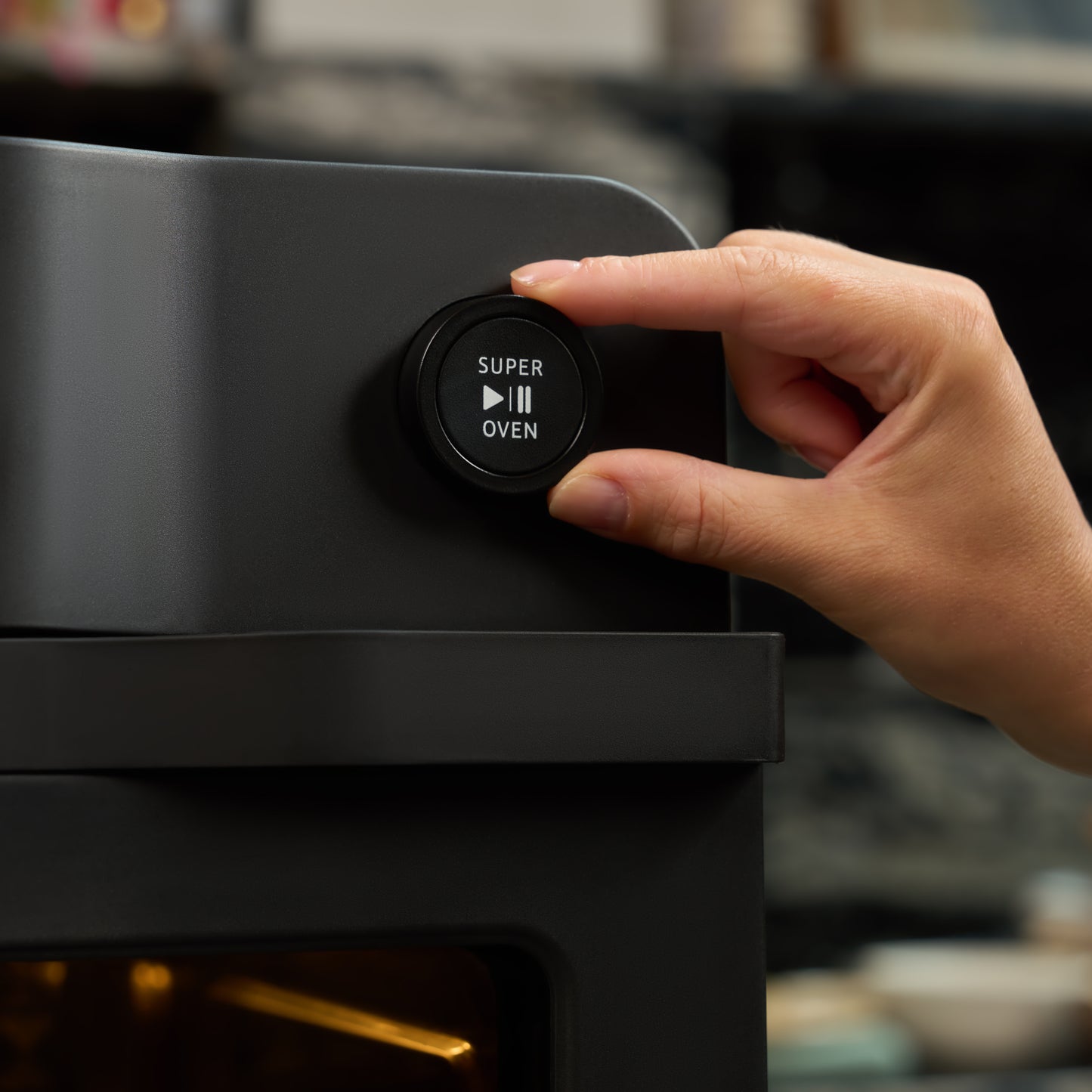 A hand is about to press a round Super Oven button with play and pause symbols on the Fridja Super Oven - 15L Digital Air Fryer Oven, a modern black appliance featuring 12 smart presets.