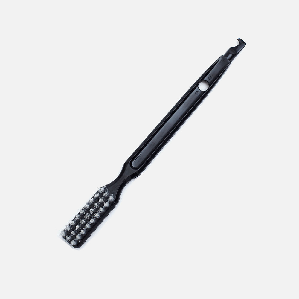 La brosse de nettoyage Fridja pour extracteurs f1900/f2500, en noir, en matériaux résistants, avec des poils d'un côté et une pointe crochet de l'autre, sur fond blanc uni.
