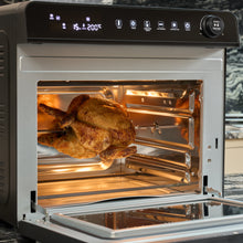 A whole rotisserie chicken roasts inside the Fridja Super Oven Pro - 30L Digital Air Fryer Oven, with the door open, interior light on, and its digital control panel clearly visible.