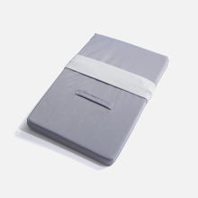 The Fridja Hand Ironing Mat is a folded gray rectangular mat with a white elastic strap and side fabric handle, offering a heat-resistant surface, shown on a plain white background.