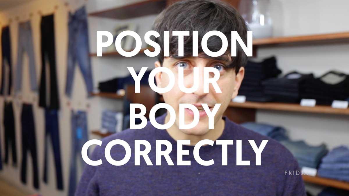 A man stands in a clothing store with folded jeans and jeans on display racks behind him. Large white text over the image reads: “POSITION YOUR BODY CORRECTLY.”.