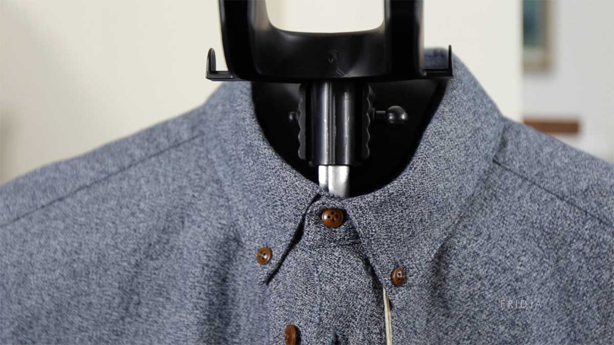 A close-up of a gray button-up shirt on a hanger or ironing tool, with the focus on the collar and buttons. The background is blurred.