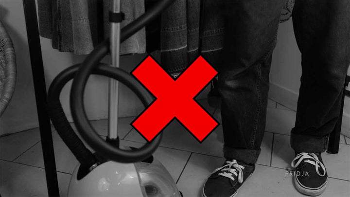A black and white image of a person standing next to a clothes steamer with a large red X symbol over it, indicating something is wrong or not recommended.