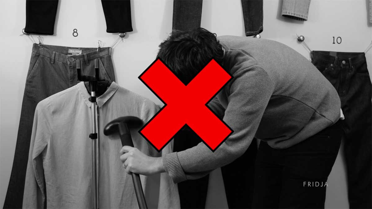 A person steams a shirt with a garment steamer; a large red X overlays the image, indicating this is not the correct method. Jeans hang on the wall in the background.