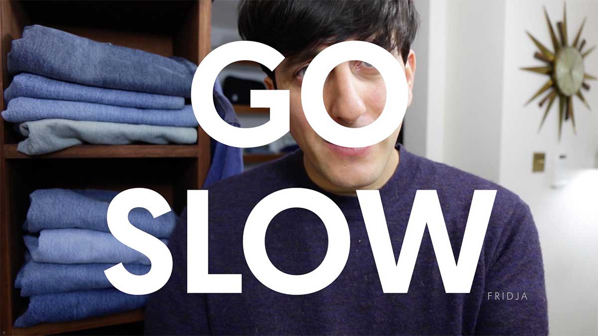A person in a dark sweater stands beside shelves of folded jeans. Large white text across the image reads GO SLOW. A star-shaped clock hangs on the wall.