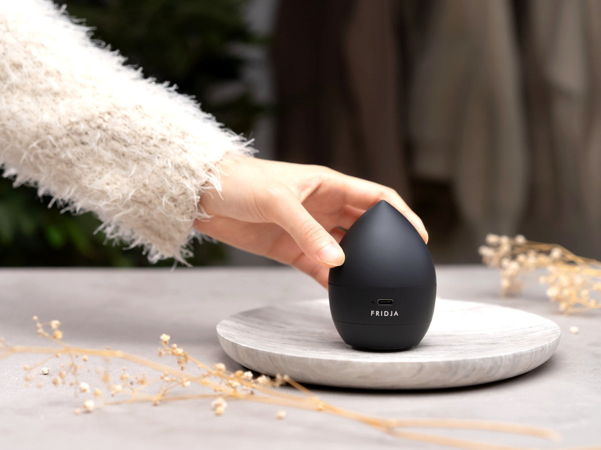 Hand in a fluffy knitted jumper placing the Fridja f40 Fabric Shaver on a stone tray