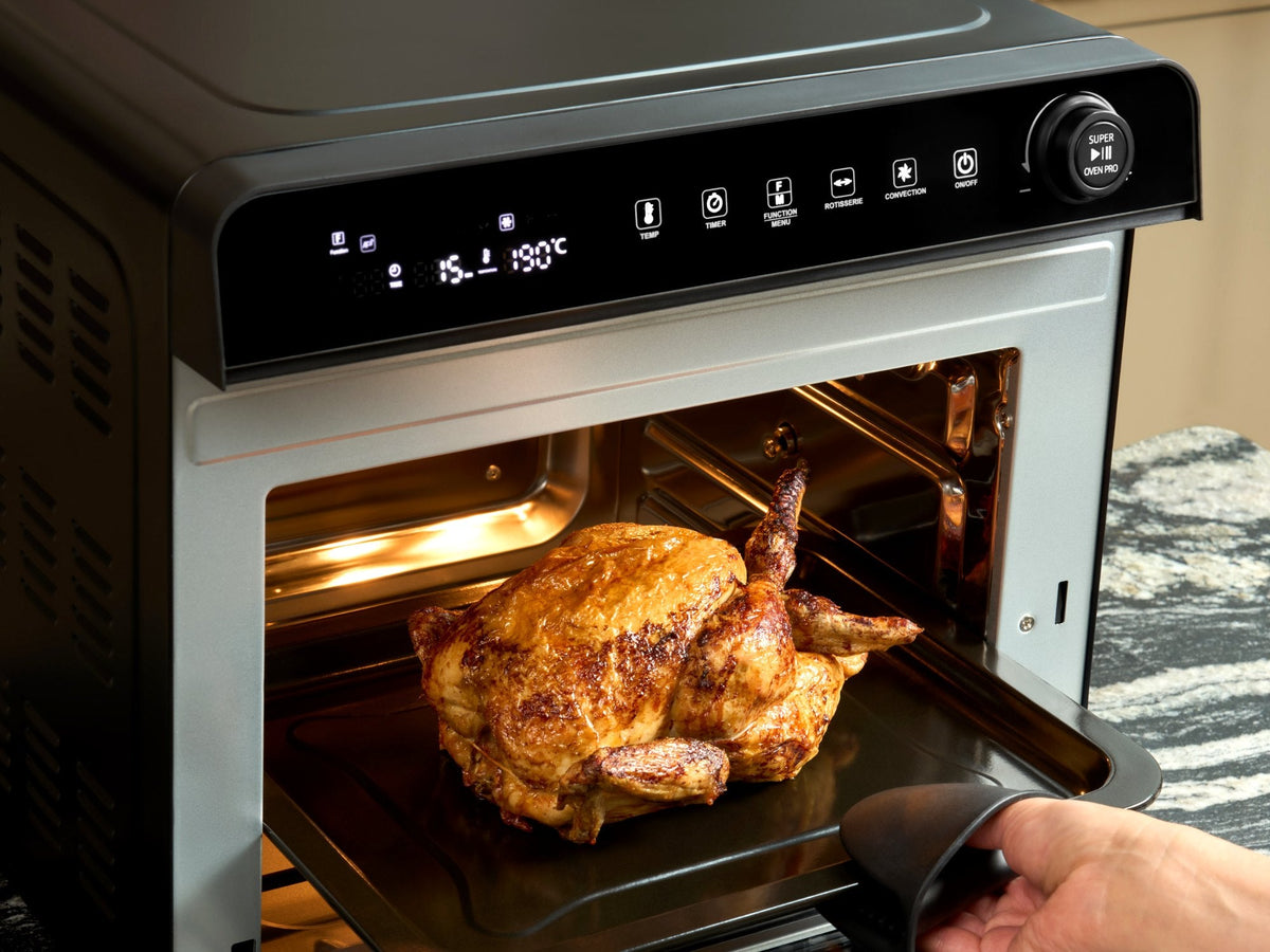 Roast chicken being lifted out of the Fridja f77 Super Oven Pro air fryer oven for a family dinner