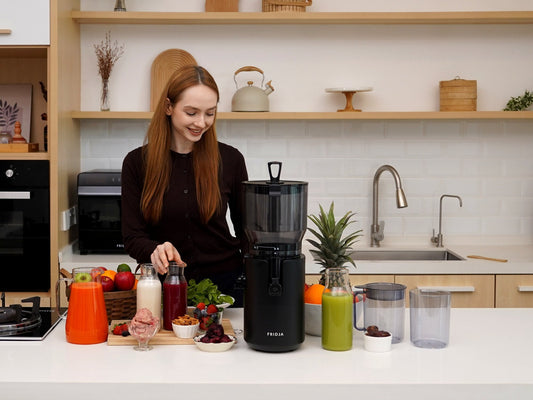 Woman preparing fresh juices in a home kitchen with the Fridja f2800 Open Whole Fruit Juicer and a jug of orange carrot juice
