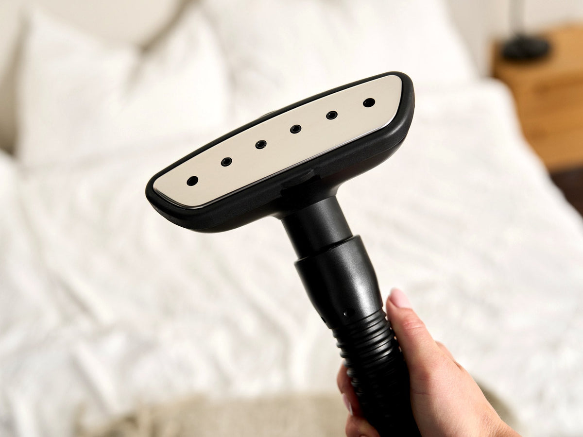 Steam head of the Fridja f1200 Clothes Steamer Pro held over fresh white bedding