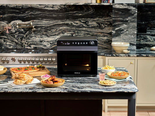 Fridja f77 Super Oven Pro air fryer oven on a kitchen island with a spread of party food