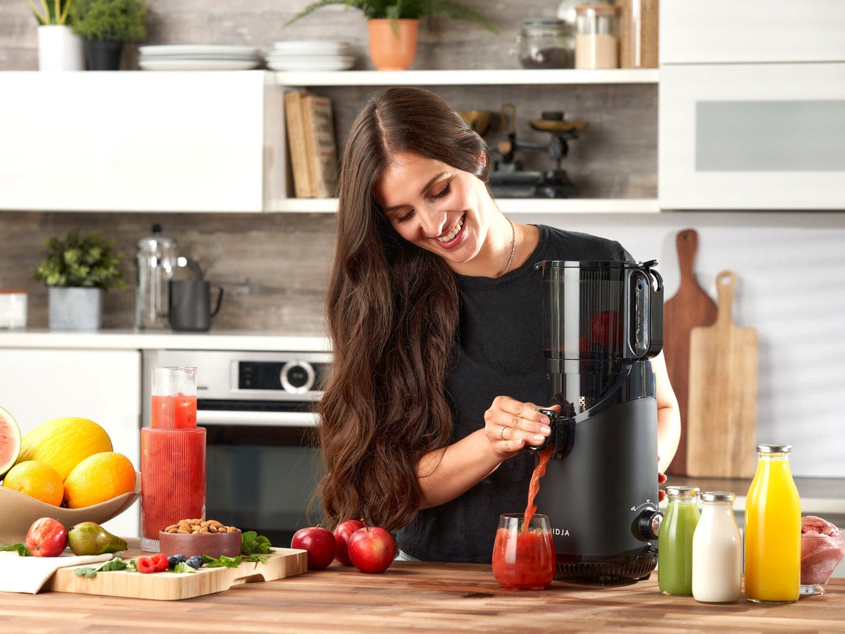 Woman pouring fresh juice into a glass from the Fridja f2500 Self Feeding Whole Fruit Juicer in a kitchen