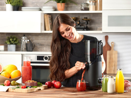 Woman pouring fresh juice into a glass from the Fridja f2500 Self Feeding Whole Fruit Juicer in a kitchen