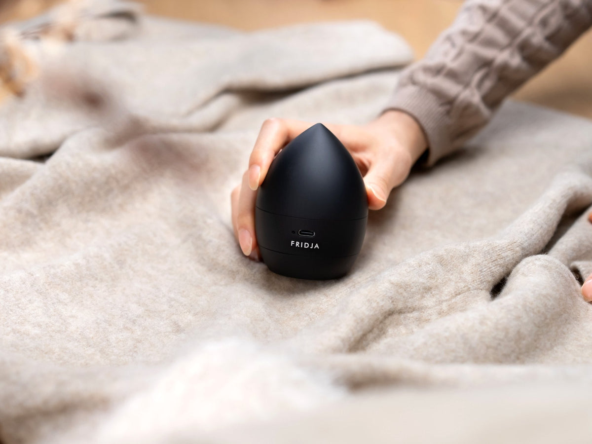 Hand using the Fridja f40 Fabric Shaver to remove lint and fuzz from a beige knitted jumper