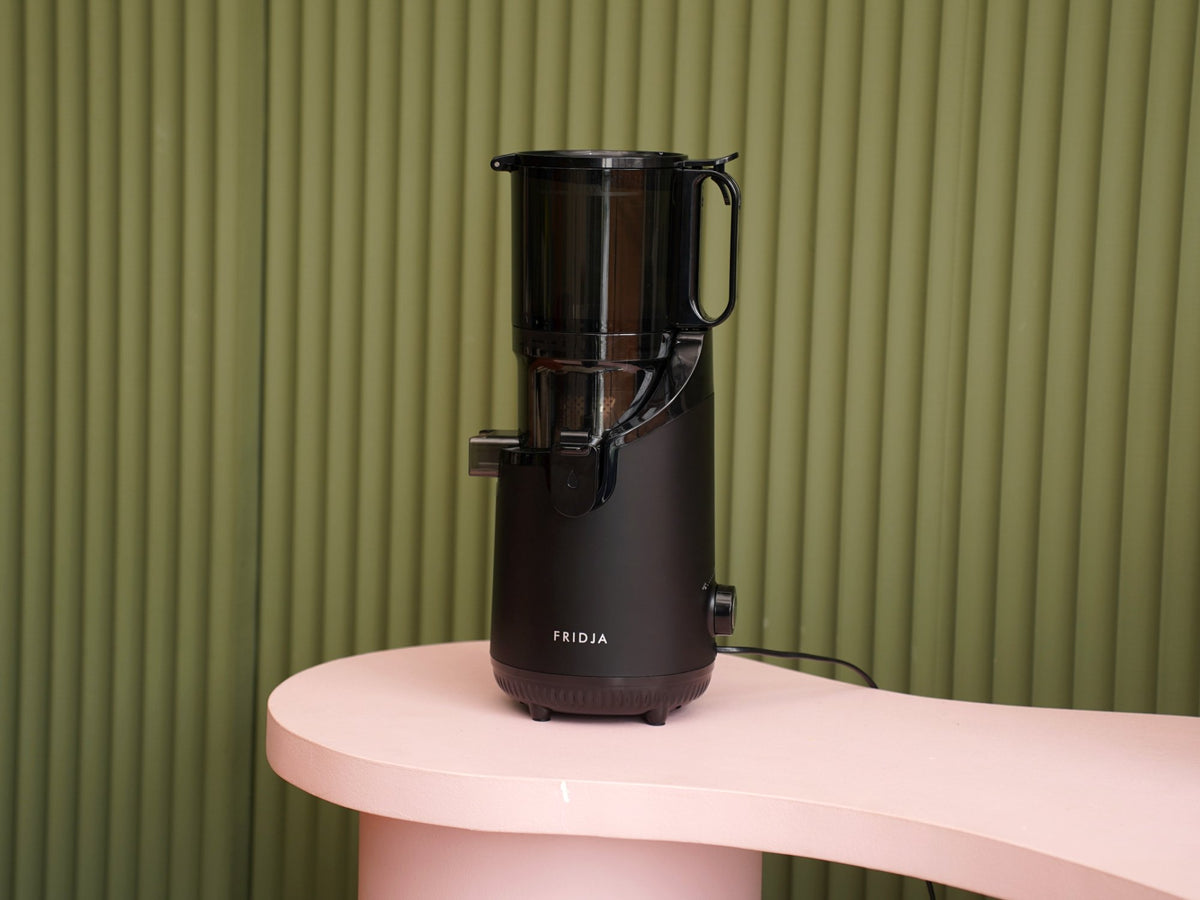 Fridja f2500 Self Feeding Whole Fruit Juicer on a pink worktop against a green panelled wall