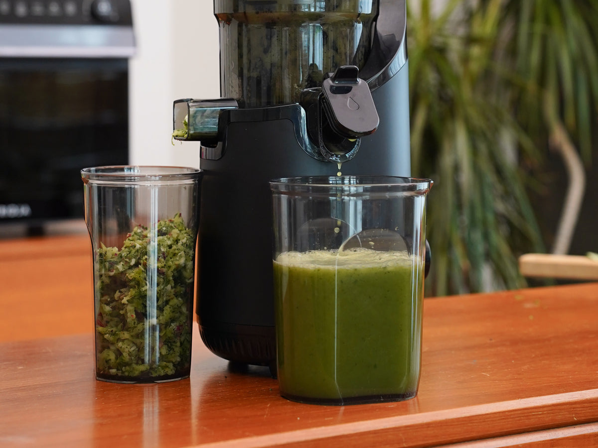 Fridja f2500 juicer pouring fresh green celery juice next to a cup of pulp