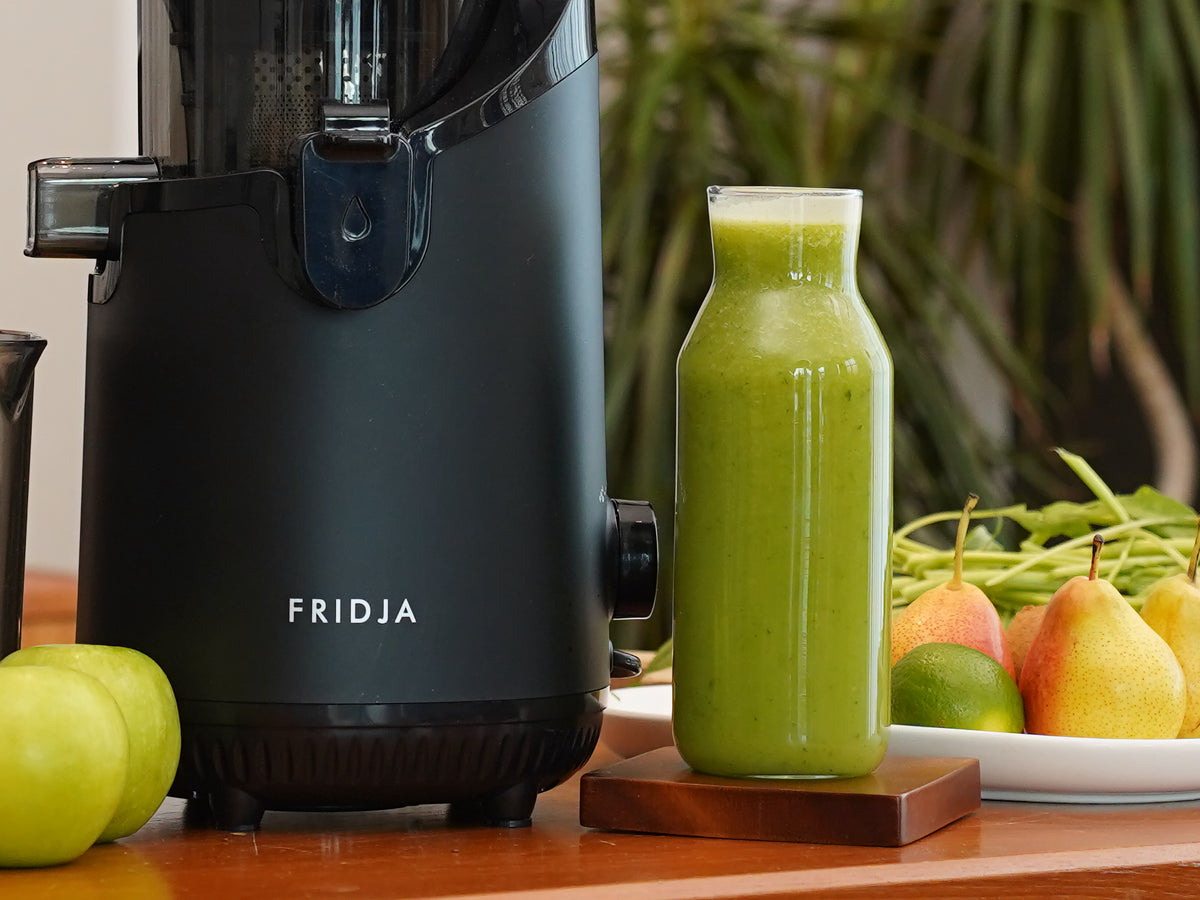 Fridja f2500 juicer beside a bottle of fresh green juice with apples and pears
