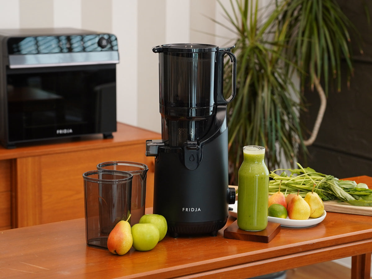 Fridja f2500 juicer on a wooden table with green juice, pears, apples and leafy vegetables