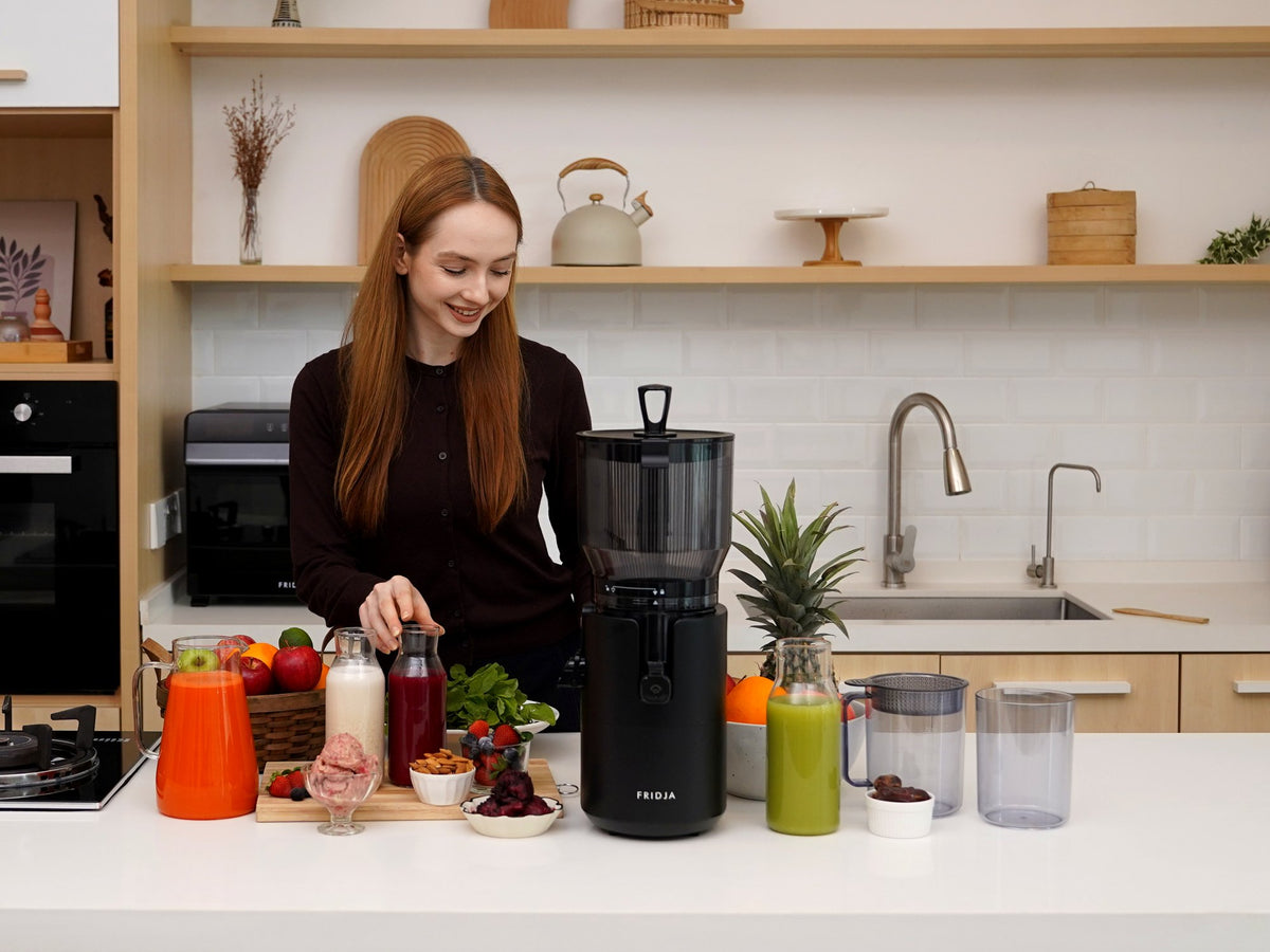 Woman preparing fresh juices in a home kitchen with the Fridja f2800 Open Whole Fruit Juicer and a jug of orange carrot juice