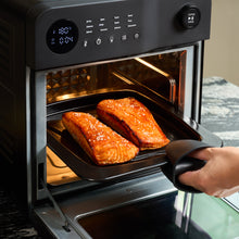 A hand in an oven mitt places a tray with two sesame-glazed salmon fillets into the Fridja Super Oven - 15L Digital Air Fryer Oven, set to 180°C for convection cooking.