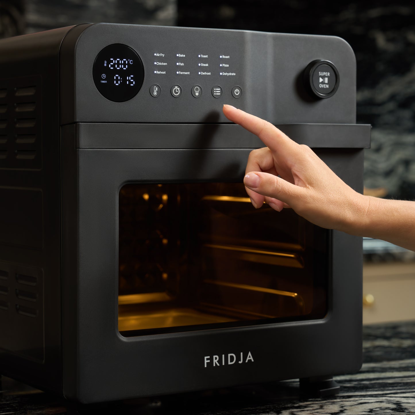 A hand presses a button on the control panel of a black Fridja Super Oven - 15L Digital Air Fryer Oven with digital display and 12 smart presets in a modern kitchen.