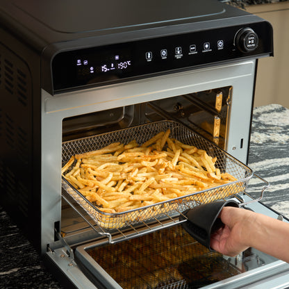 A hand uses a potholder to pull out a basket of cooked French fries from the Fridja Super Oven Pro - 30L Digital Air Fryer Oven, which features a sleek digital display like a convection oven.