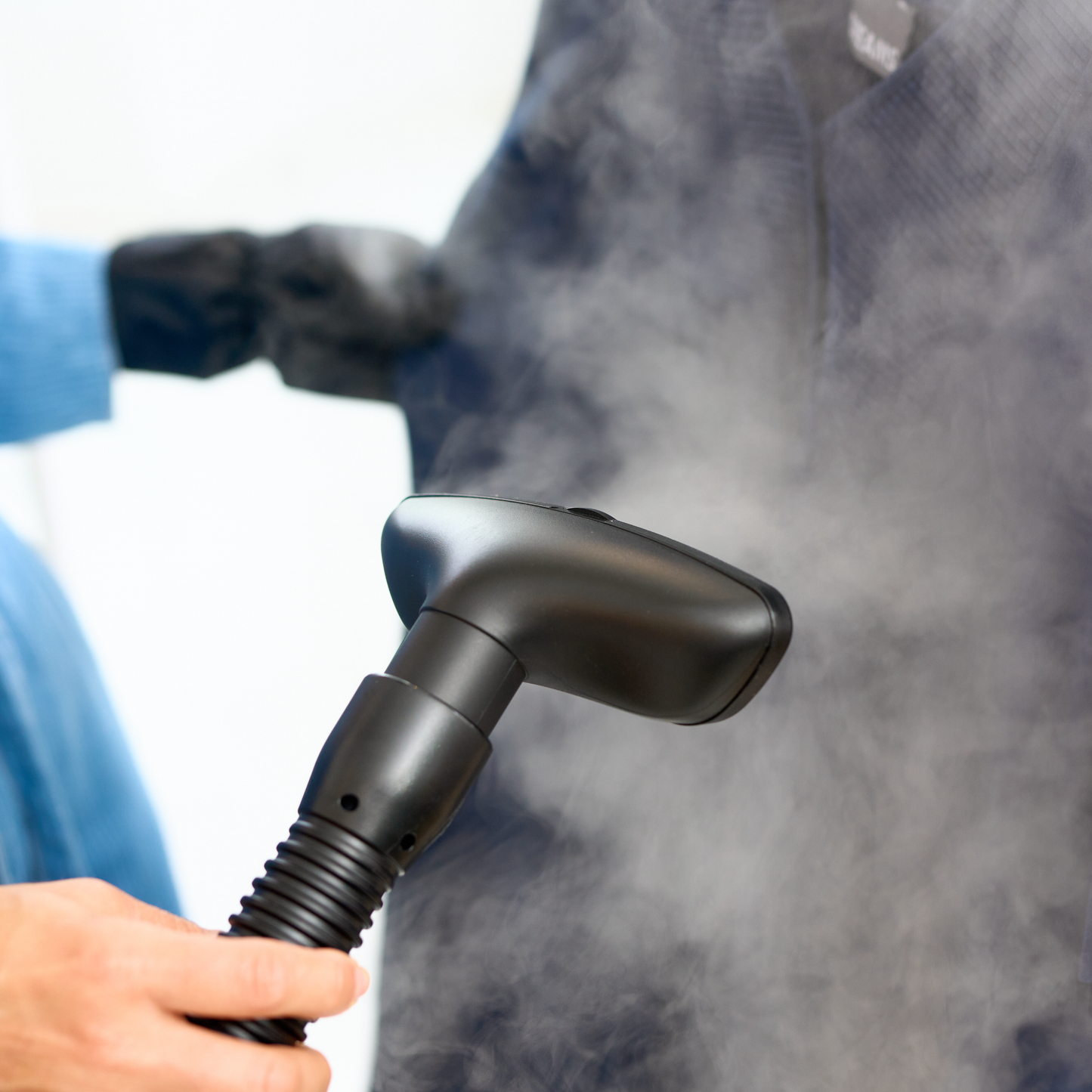 A person uses the Fridja f1600 Commercial Clothes Steamer to remove wrinkles from a dark garment, with steam rising for expert garment care.