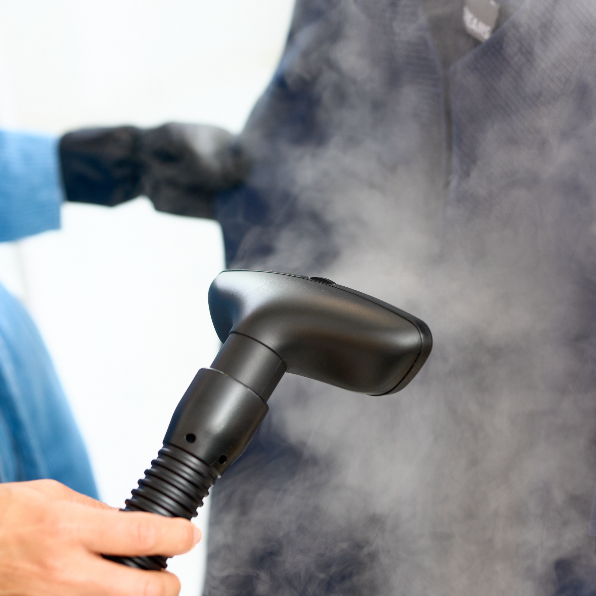 A person uses the Fridja f1600 Commercial Clothes Steamer to remove wrinkles from a dark garment, with steam rising for expert garment care.