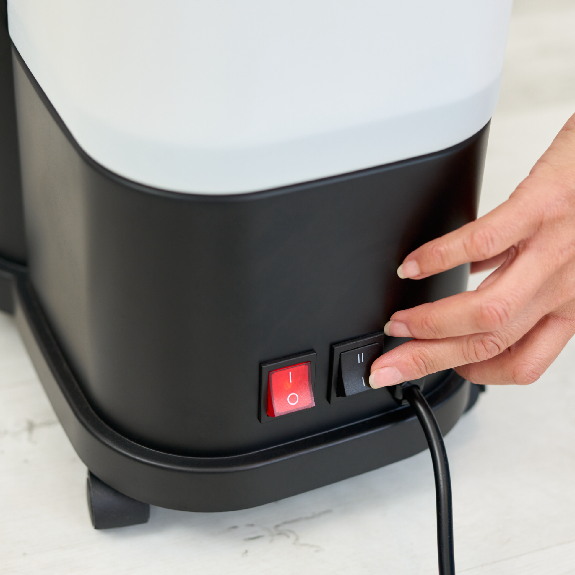 A hand presses the black power switch beside a red switch on the Fridja f1600 Commercial Clothes Steamer, with its power cord plugged in—perfect for efficient garment care.
