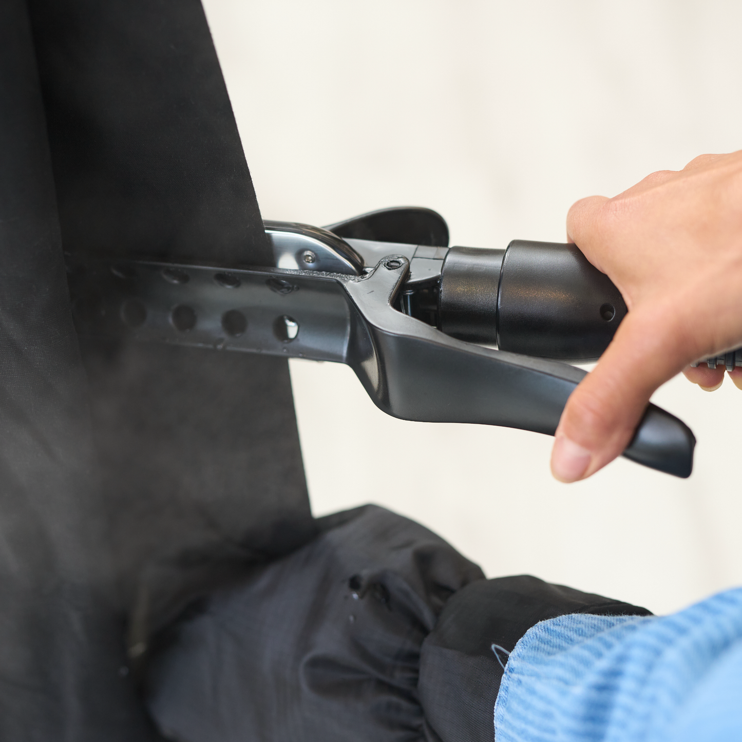 A person uses the Fridja f1600 Commercial Clothes Steamer to remove wrinkles from black fabric, with steam emerging near the nozzle. Their hand and blue sleeve are visible, showcasing effective garment care in action.
