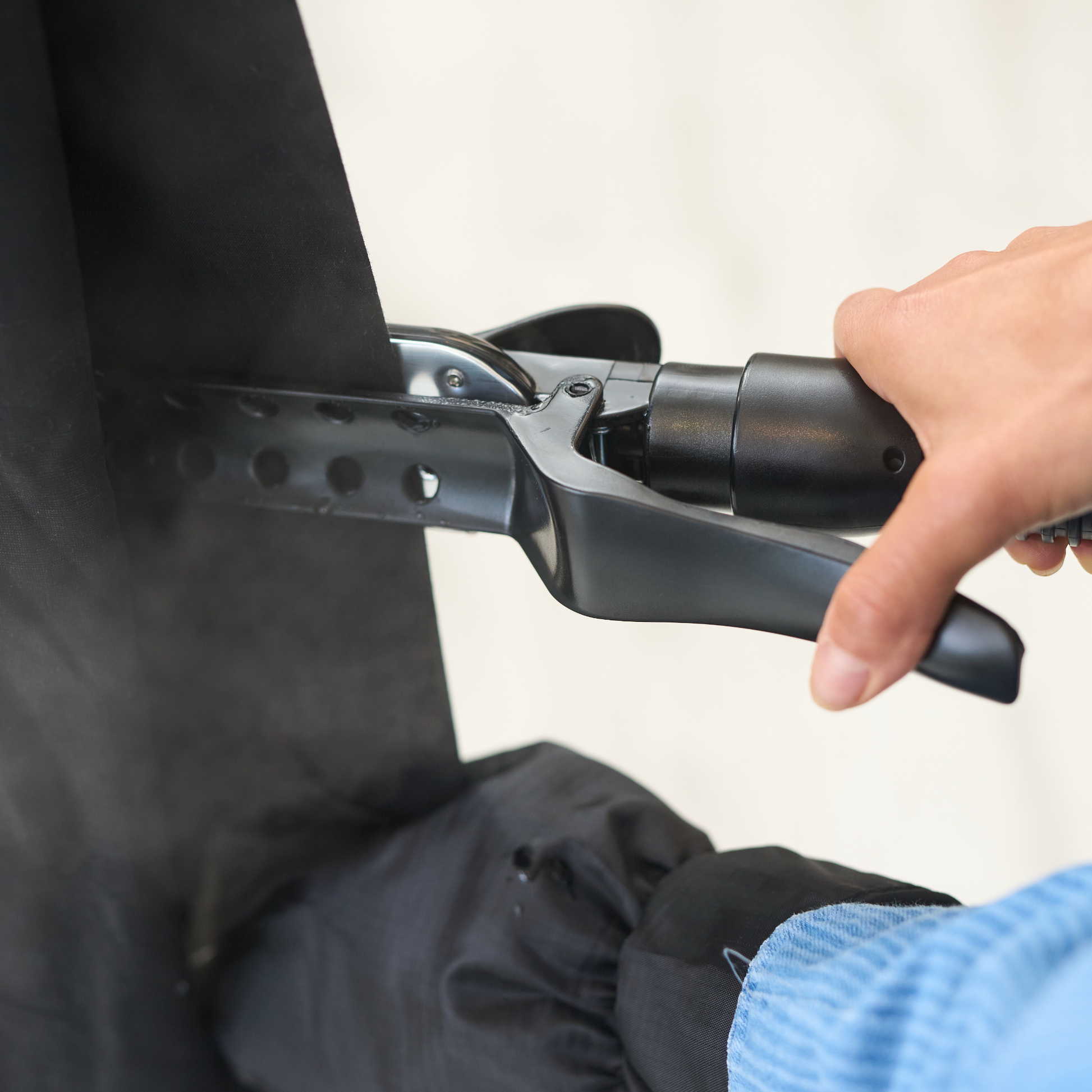 A person uses the Fridja f1600 Commercial Clothes Steamer to remove wrinkles from black fabric, with steam emerging near the nozzle. Their hand and blue sleeve are visible, showcasing effective garment care in action.