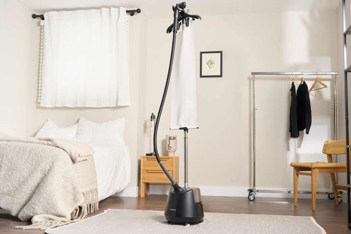 Fridja f1200 Clothes Steamer Pro in matt black standing in a bedroom