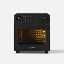 The Fridja f66 Super Oven is a black countertop oven with a digital display, control buttons, and a knob. It features an illuminated interior and textured oven wall visible through its glass door.
