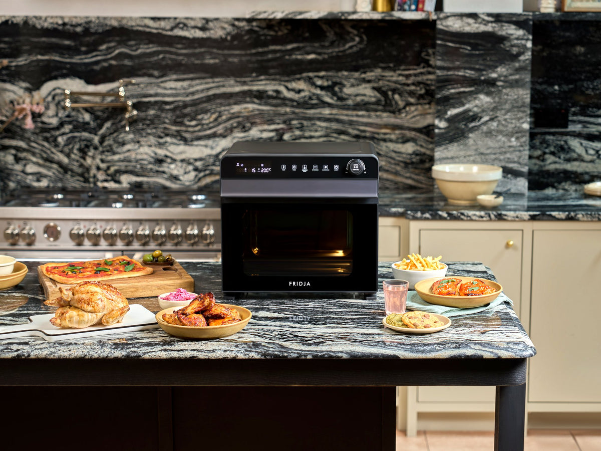 Fridja f77 Super Oven Pro air fryer oven on a kitchen island with a spread of party food