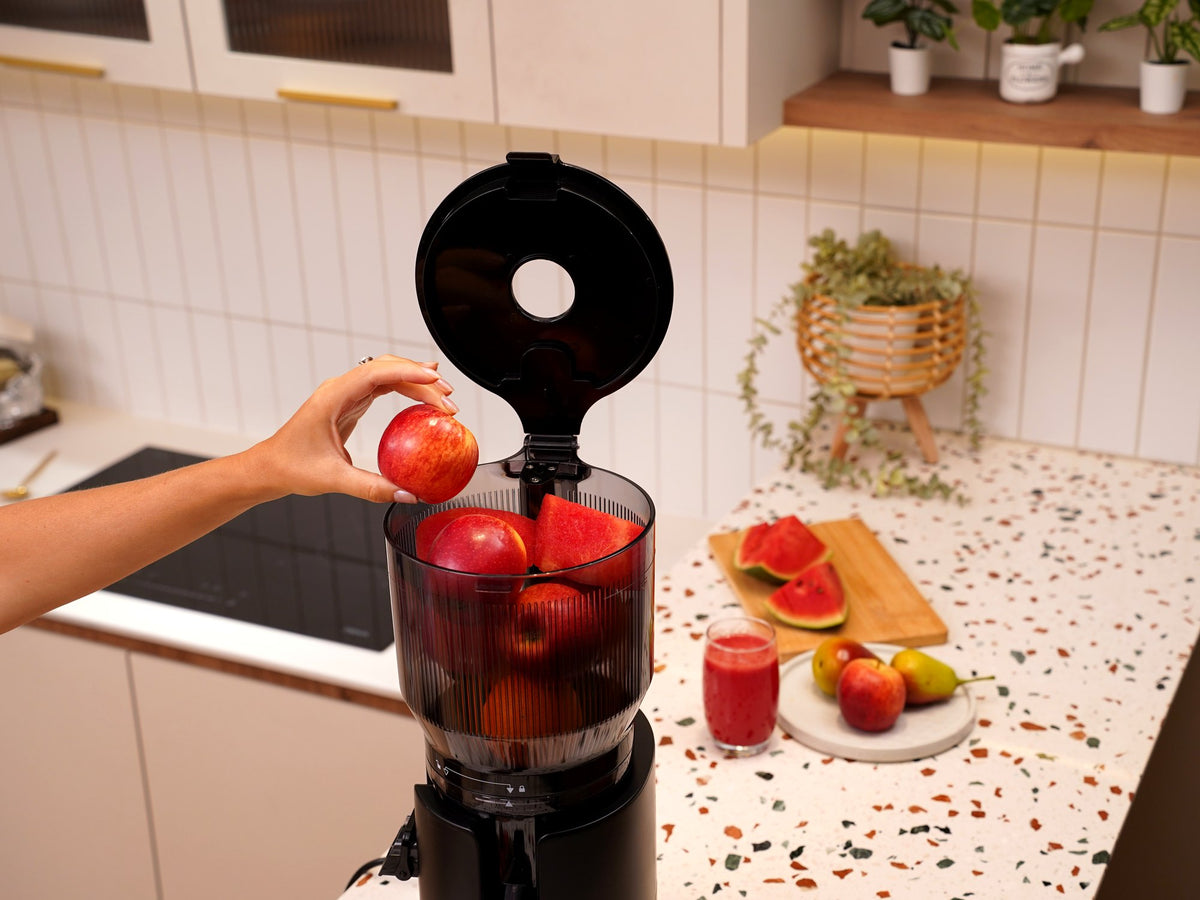 Whole apple being dropped into the open chute of the Fridja f2800 Open Whole Fruit Juicer to make homemade apple juice