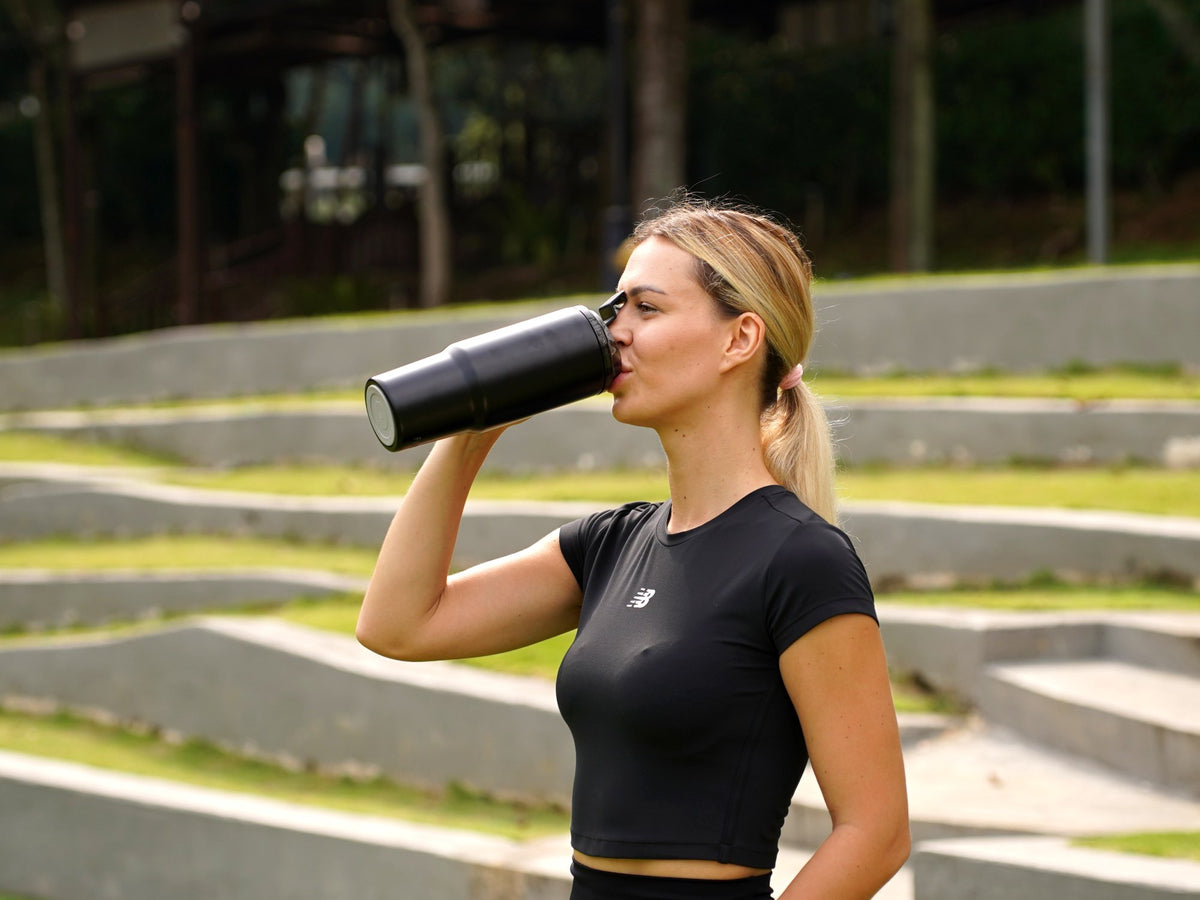 Woman in gym wear drinking from the Fridja f600 Stainless Steel Portable Blender outdoors
