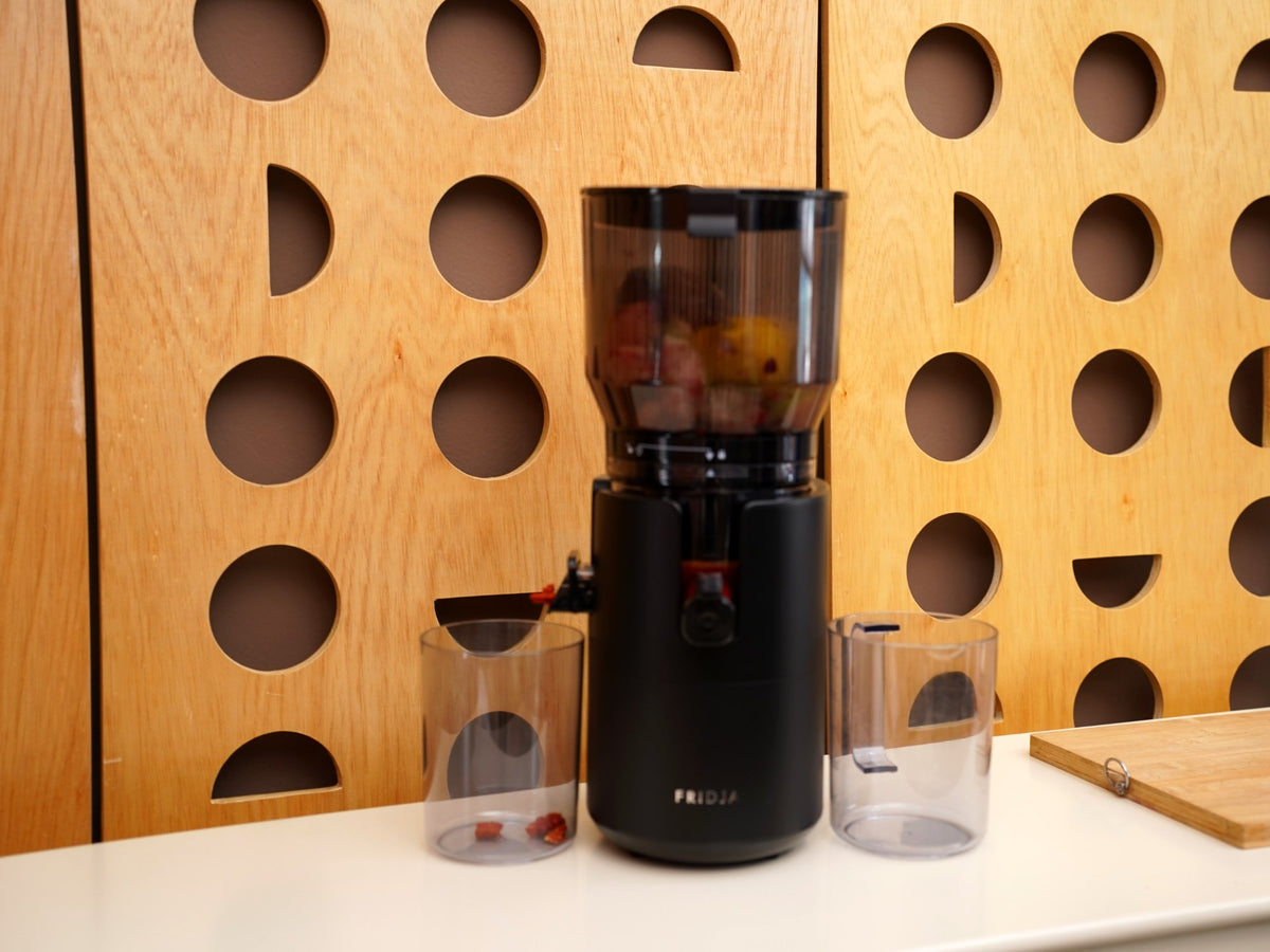 Fridja f2500 Self Feeding Whole Fruit Juicer loaded with whole fruit, with juice and pulp jugs on a white worktop