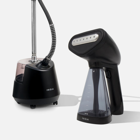 Two black Fridja Garment Care Steamer Duo models—the f1200 Clothes Steamer Pro with hose and tank, and the f10 Handheld with transparent reservoir—are shown on a light background, ideal for wrinkle-free garments.