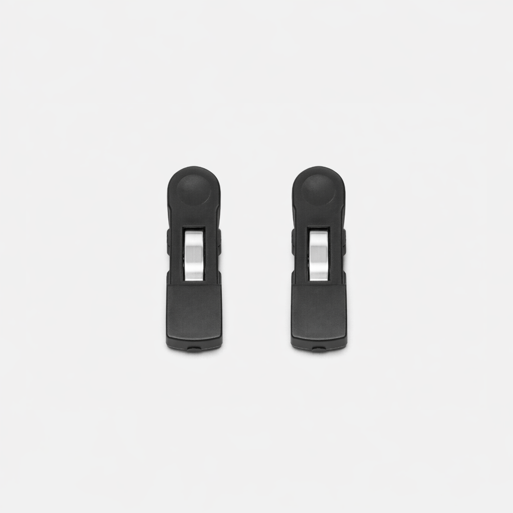 Two identical Fridja f1200 Clips, made of black plastic with silver metal springs, are arranged vertically side by side on a white background as replacement parts for the Clothes Steamer Pro.