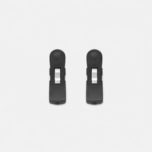 Two identical Fridja f1200 Clips, made of black plastic with silver metal springs, are arranged vertically side by side on a white background as replacement parts for the Clothes Steamer Pro.