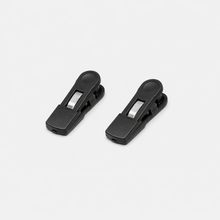 Two black plastic spring clips with silver metal hinges from Fridja are shown side by side on a plain white background—ideal as f1200 Clips or replacement parts for the f1200 Clothes Steamer Pro.