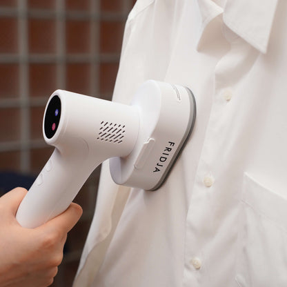 A person uses the Fridja f20 Handheld Clothes Steamer Pro with Suction to effortlessly remove wrinkles from a white button-up shirt, demonstrating the convenience of this portable iron alternative.