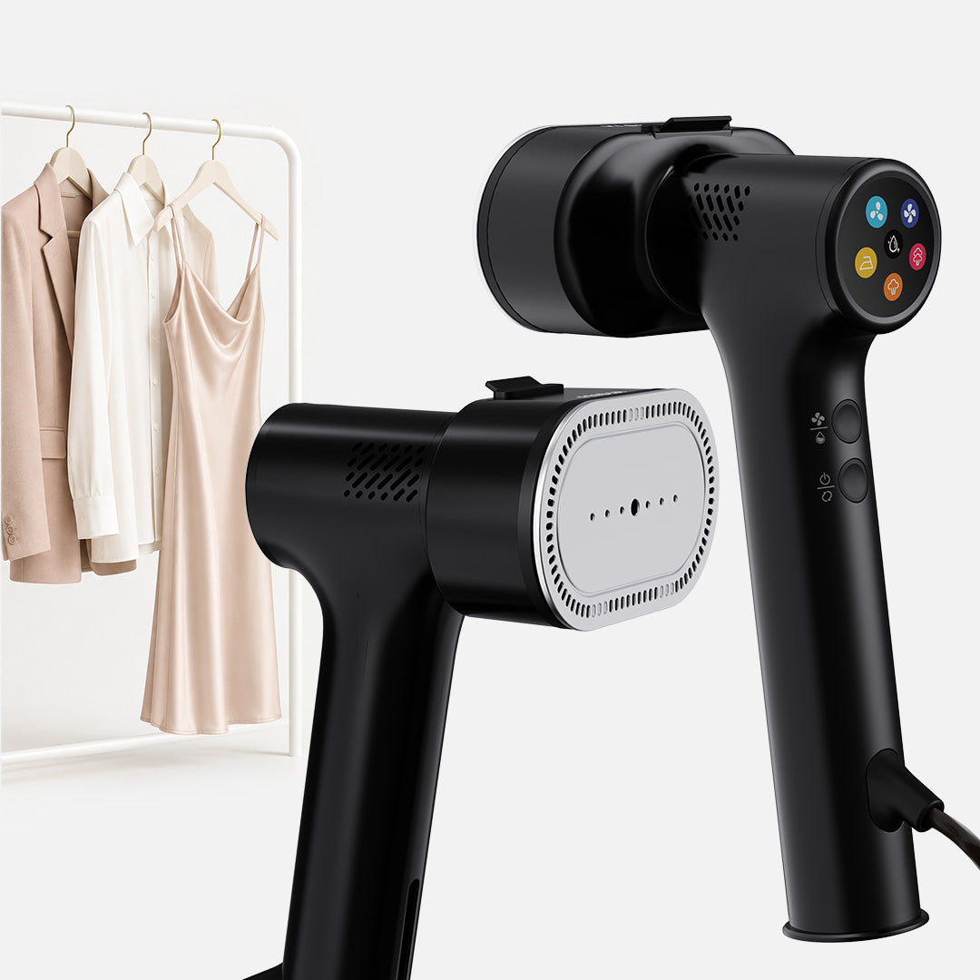 The Fridja f20 Handheld Clothes Steamer Pro with Suction, a sleek black appliance with convenient control buttons and shown from two angles, stands in front of a rack displaying a white blouse, beige blazer, and satin slip dress—offering a modern alternative to the traditional iron for gently smoothing delicate garments.