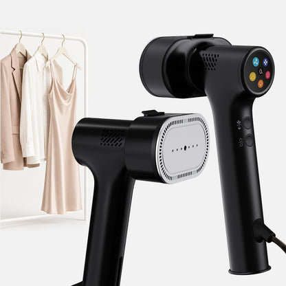 The Fridja f20 Handheld Clothes Steamer Pro with Suction, a sleek black appliance with convenient control buttons and shown from two angles, stands in front of a rack displaying a white blouse, beige blazer, and satin slip dress—offering a modern alternative to the traditional iron for gently smoothing delicate garments.
