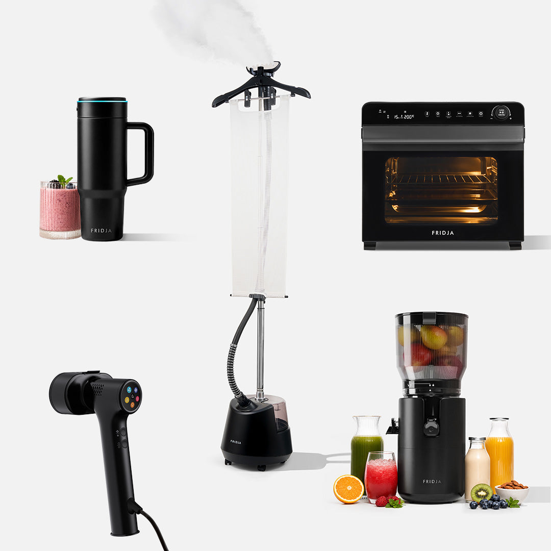 Five black Fridja Full Range Deluxe appliances on a white background: the f600 Stainless Steel Portable Blender with smoothies, the f1200 Clothes Steamer Pro releasing steam, the f77 Super Oven Pro air fryer oven, the f20 Handheld Clothes Steamer Pro, and the f2800 Open Whole Fruit Juicer with juice and fruit beside it.