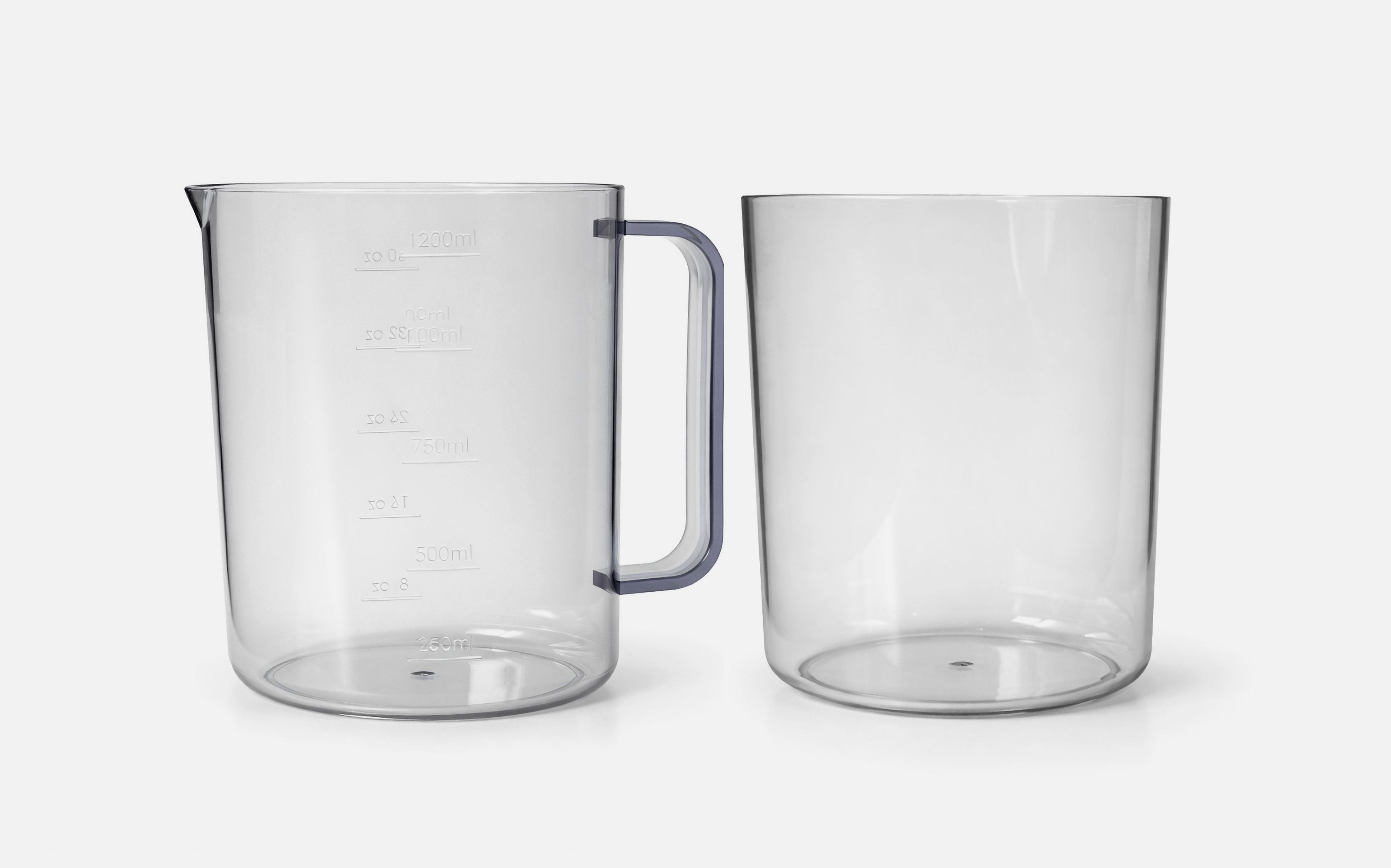 Two transparent plastic measuring jugs are side by side on a white background; the left jug has a handle and measurement markings, while the right jug has no handle or markings.