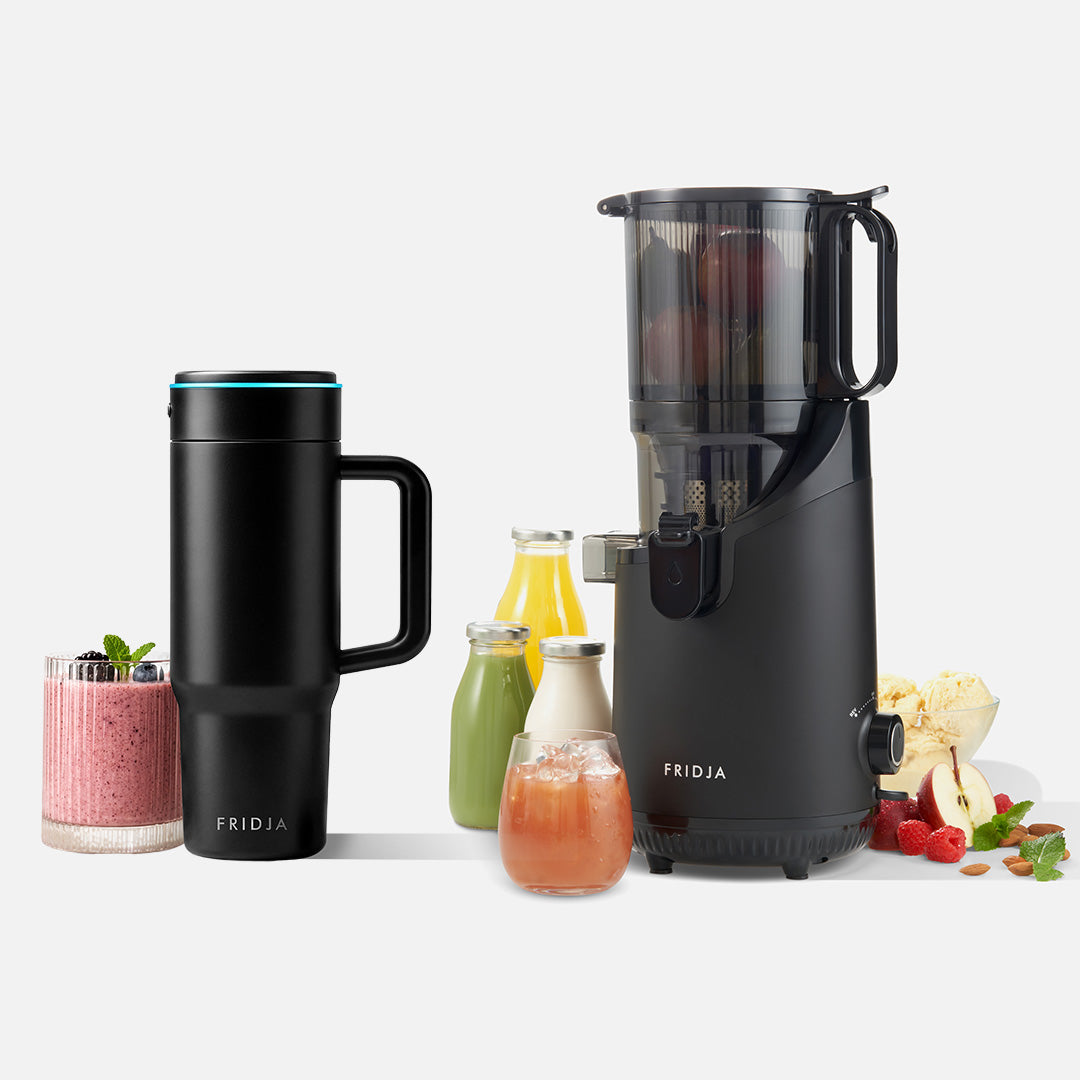 A Fridja Juicer Duo – f2500 Self Feeding Whole Fruit Juicer in black is displayed alongside fresh fruits, juice bottles, a smoothie, a sleek black Fridja f600 Stainless Steel Portable Blender (travel mug), and a glass of juice on a white surface.
